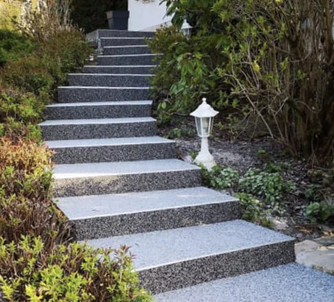 Escalier extérieur en béton désactivé avec contremarches blanches lisses, bordé de végétation luxuriante et éclairé par une lanterne décorative blanche