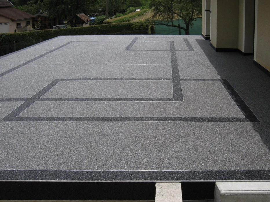 Terrasse extérieure résidentielle avec revêtement en résine granulat gris clair délimité par des bandes décoratives anthracite formant un motif géométrique rectangulaire