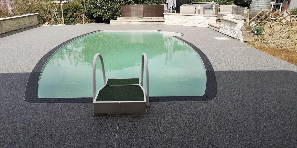 Chantier extérieur avec piscine enterrée de forme ovale à l'eau verte, équipée d'un escalier central métallique avec main-courantes