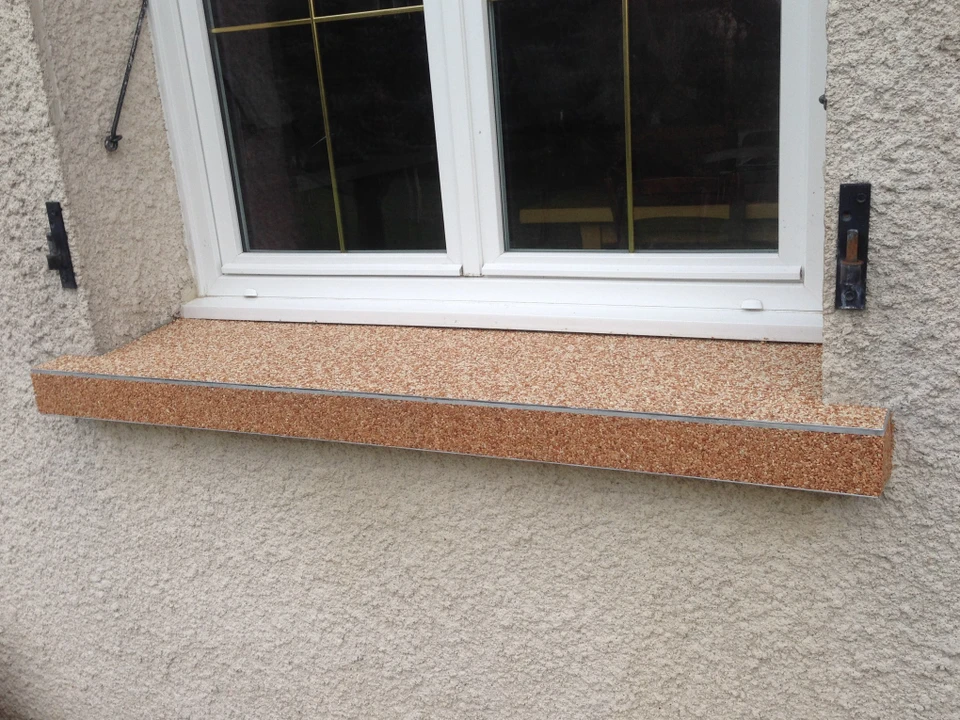 Jardin paysager avec pelouse verte, massif végétal délimité par bordure de galets blancs décoratifs, allée carrelée avec caniveau à grille métallique, pot en terre cuite contenant plantes aquatiques