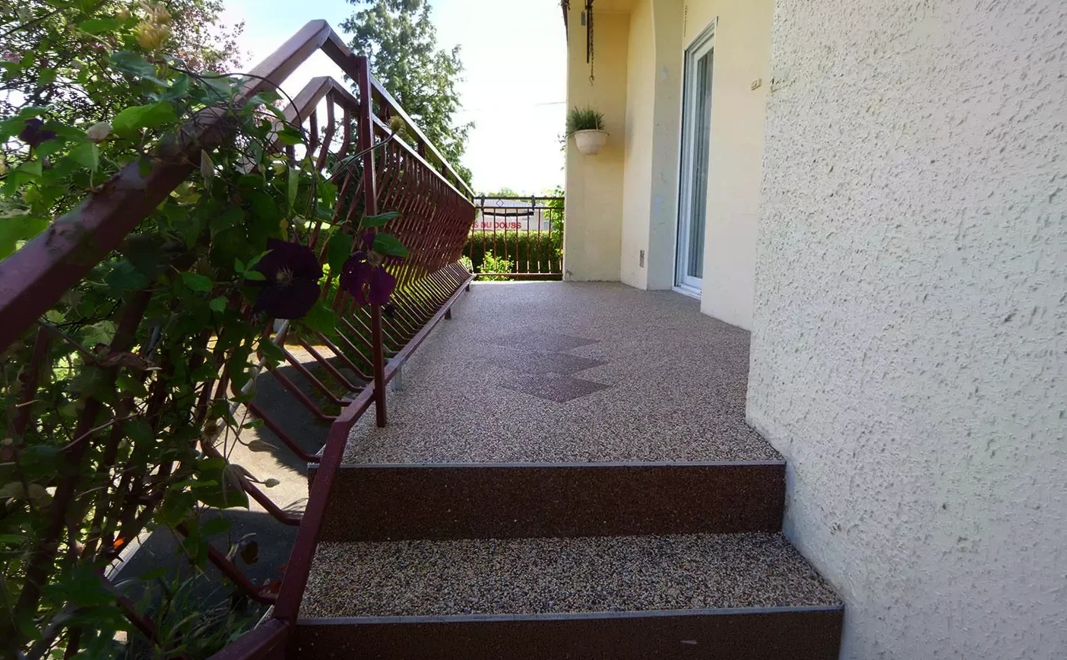 Balcon d'appartement avec deux fauteuils en résine tressée et coussins beiges, planchers en composite, garde-corps métallique noir